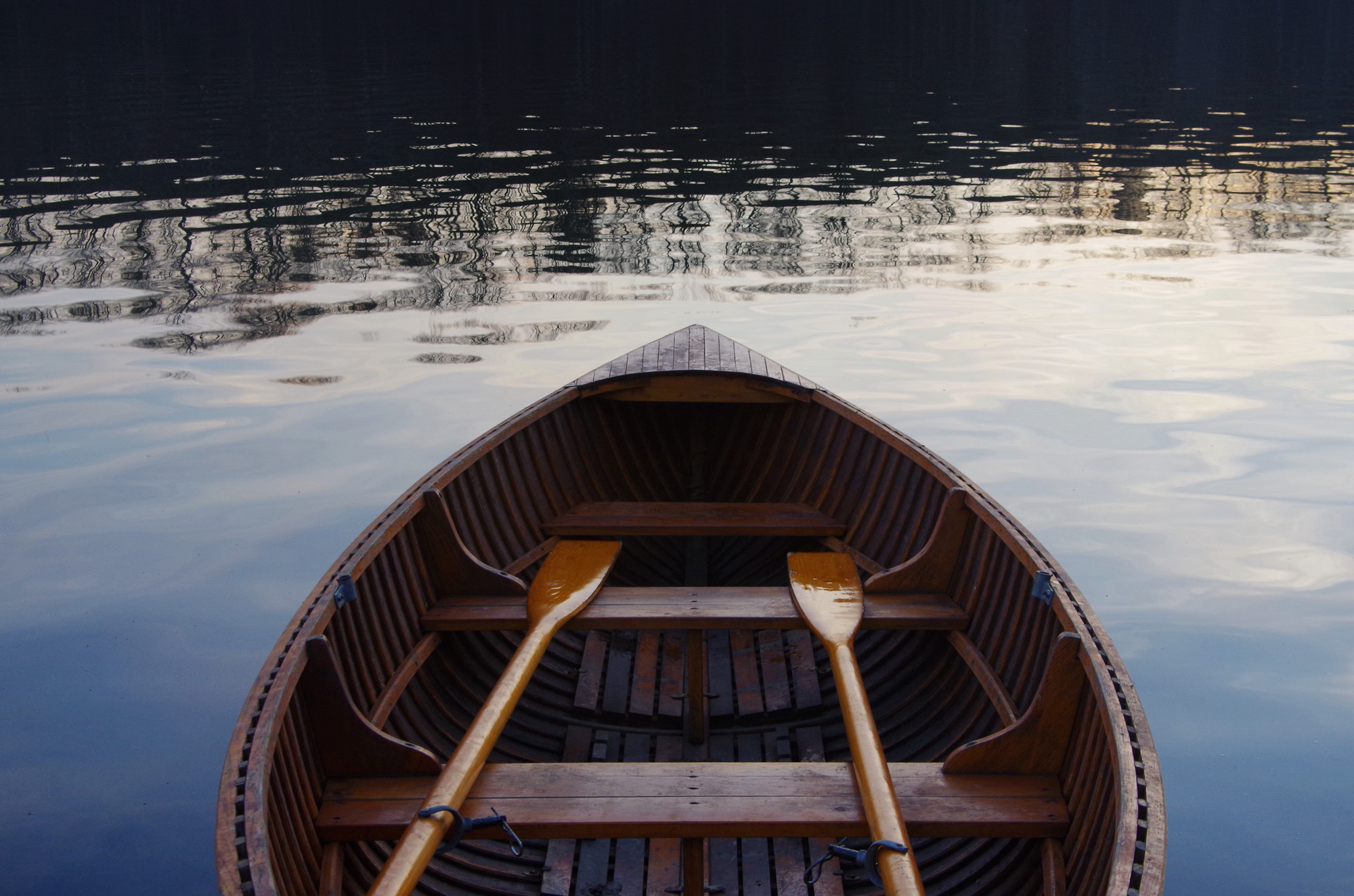 A rowing boat and oars on a lake with the landscape reflecting on the water.
